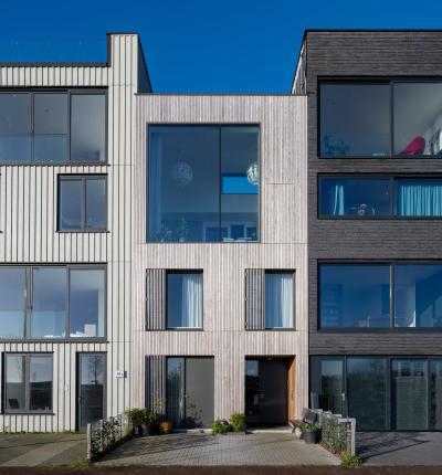 Voorgevel van houten stadswoning op Zeeburgereiland, onderdeel van rij zelfbouwwoningen met grote ramen.