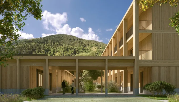 Nieuwbouw met houten gevels en overdekte doorgang, gelegen in een groene bergomgeving met bomen, struiken en een helderblauwe lucht op de achtergrond.